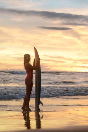 Young female with a surfboard at sunset