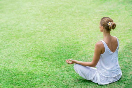 Young woman in a lotus pose on lawnの写真素材