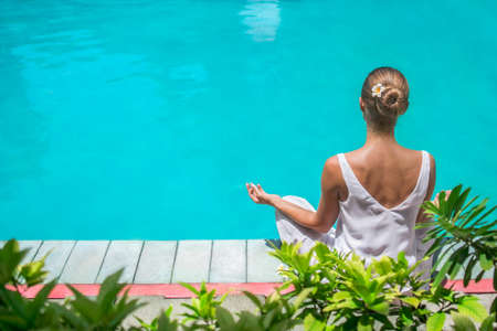 Young woman in a lotus pose by the poolの写真素材