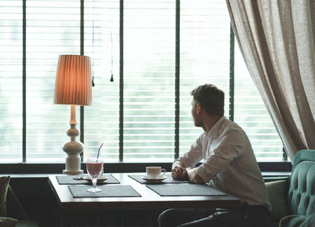 Young man with a cup of coffee by the windowの写真素材