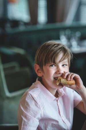 Little smiling boy eating pie in a cafeの写真素材