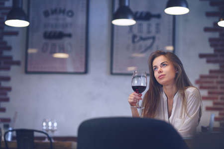 Young attractive girl with a glass of wine in a restaurantの写真素材