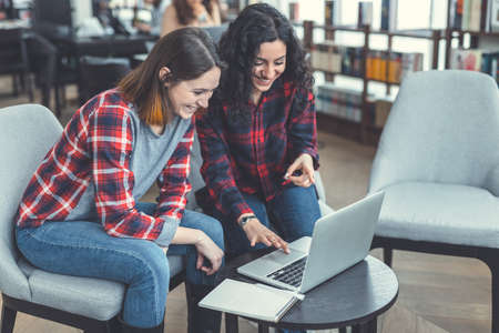 Smiling girls with laptop in a bookstoreの写真素材