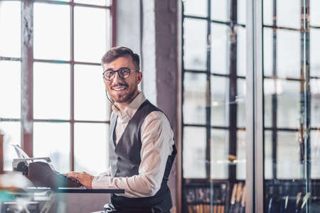Smiling young man with a retro typewriter indoorsの写真素材