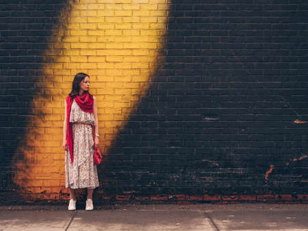 Attractive girl with a red scarf by the bright wallの写真素材