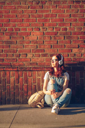 Young girl listening to music at a brick wall at sunsetの写真素材