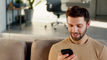 Attractive man with smartphone at home. Handsome man using phoneの写真素材