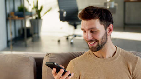 Attractive man with phone on sofa. Smiling student with smartphone at homeの写真素材