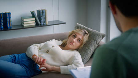 Young woman on the couch talking about her problem to the psychiatrist at therapy. A young woman on the couch tells the psychologist about the problems.の写真素材