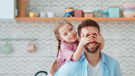 A little preschool girl covers her dad's eyes with her hands. Young family having funの写真素材