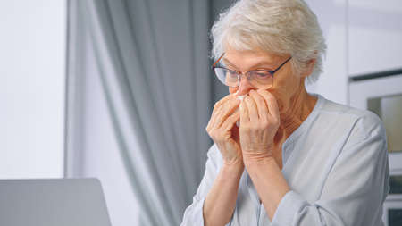Ill aged secretary with gray hair wipes red nose with white paper napkin and types on laptop at home isolation close viewの写真素材