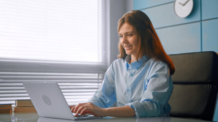 Professional medical worker brunette with long loose hair types on gray laptop and smiles cheerfully sitting at table in officeの写真素材