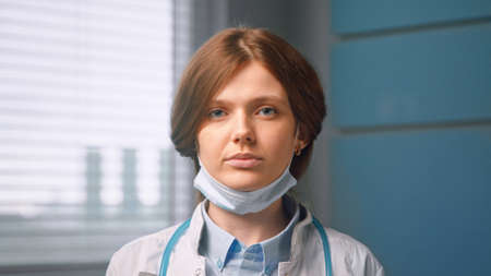Young woman general practitioner looks straight against blue hospital room wall close viewの写真素材