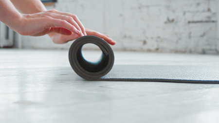Woman hands roll gray rubber mat to train on parquet floor in spacious light yoga studio extreme close viewの写真素材