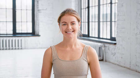 Attractive blonde young woman wearing stylish light beige tracksuit smiles to camera standing in spacious yoga studio close viewの写真素材
