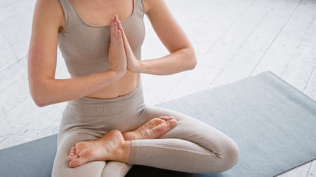 Motion past lady yoga practitioner in new beige tracksuit sitting in lotus position with namaste on mat in light studio closeupの写真素材