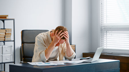Upset financial director reads bank reports sitting at gray table and calculator in officeの写真素材