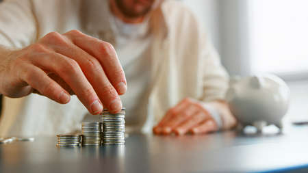Blurry guy bank white collar gathers silver coins in piles on office table with piggy bank silhouette closeの写真素材