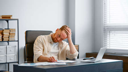 Young male financial director reads bank reports sitting at gray table and calculator in office near large windowの写真素材