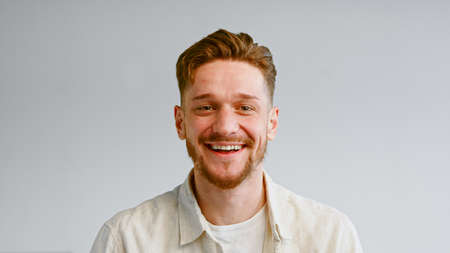 Portrait of serious bearded guy in yellow shirt looking straight and then smiling cheerfully on white wall background closeupの写真素材