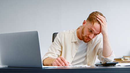 Concentrated and worried manager looks at paper checks and total sum on calculator and puts head in...