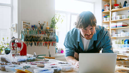 Young master typing a message on a laptop in the studio. Man in an apron surfing the internet using a laptopの写真素材