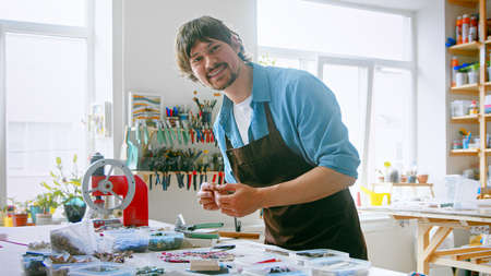 A young master in an apron at work in his workshop. Smiling young man looking at the cameraの写真素材