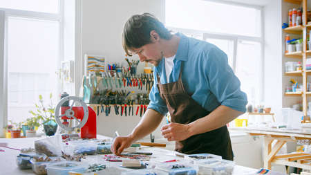 Young master in an apron at work in his workshop. Working man with mosaic in studioの写真素材