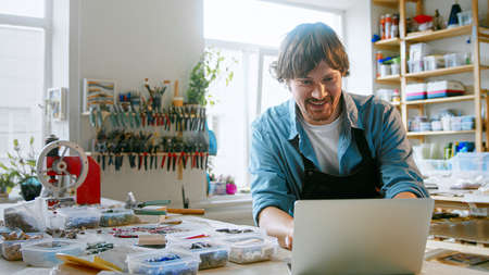 Smiling man typing on laptop in mosaic workshopの写真素材