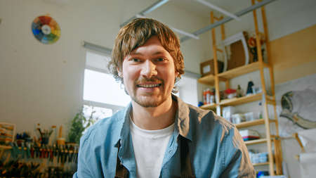 Smiling master looking at camera talk make live video conference call online in the workshop. Young man close up, webcam viewの写真素材