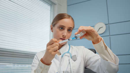 Young woman medical blogger in white coat shows syringe in hospitalの写真素材