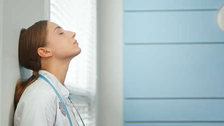Young woman doctor breathes deeply leaning on wall closeupの写真素材