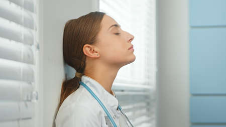 Attractive woman doctor breathes deeply leaning on wall closeupの写真素材