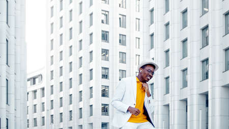 Black man performs contemporary dance with cheerful smile on gray city street pavement among highrise city buildings on sunny dayの写真素材