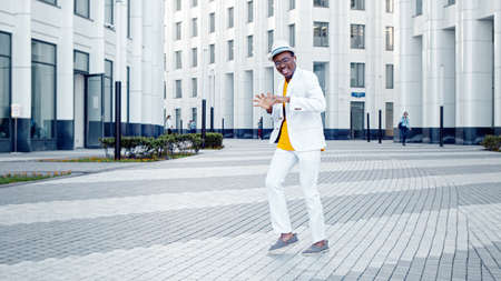 Professional African American dancer in suit and hat performs on gray square pavement among highrise megalopolis office buildingsの写真素材