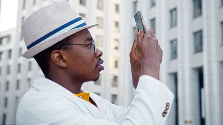 African American guy in white classic suit makes panoramic photo of highrise office buildings on megalopolis street close viewの写真素材