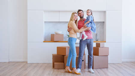 Amazed family parents and little funny daughter bring brown cardboard boxes on large pile on floor and pose in new apartmentの写真素材