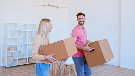 Amazed couple man and lady walk along new apartment room holding large cardboard boxes putting on pile and smiling cheerfullyの写真素材