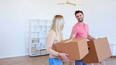 Couple of guy and blonde lady holds cardboard boxes and puts on large pile in new apartment after moving with happy smilesの写真素材