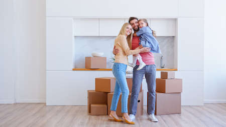 Little funny preschooler girl brings cardboard box on large pile and jumps in bearded father arms near mother in new flatの写真素材