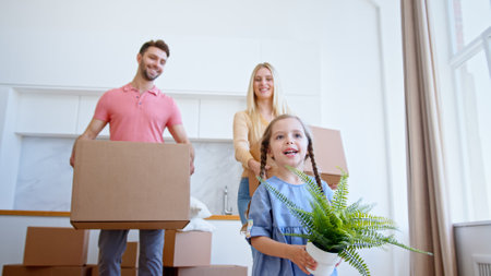 Funny little preschooler daughter looks at parents walking along new apartment with green pot plant and happy smile low angle shotの写真素材