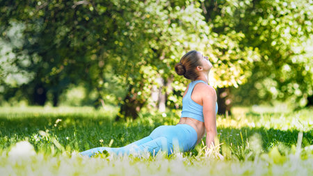 Professional athlete lady blonde in blue tracksuit performs yoga exercise changing asanasの写真素材