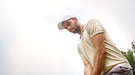 Young golfer in a cap hitting a golf ball with a golf club on the background of the skyの写真素材