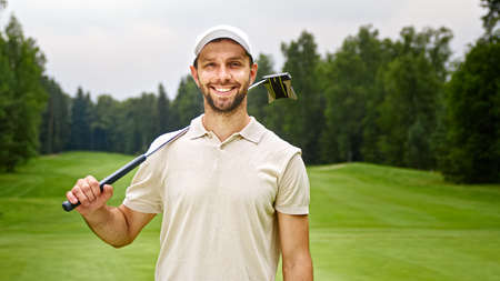 Young man with golf club looking at camera at golf course outdoorsの写真素材