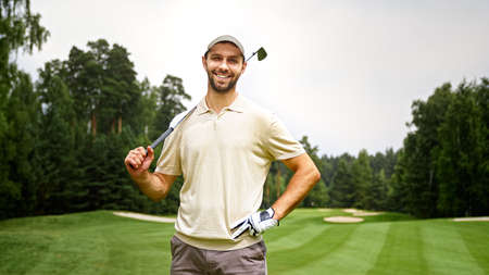 Young man with golf club looking at camera at golf courseの写真素材