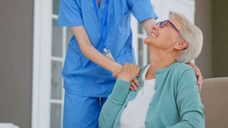Caretaker hugs positive single mature gray haired lady in spacious room at long term care homeの写真素材