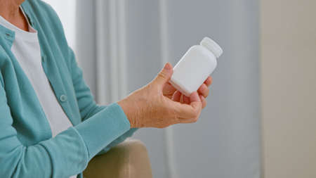 Mature woman patient takes blank white bottle of medicine from doctor sitting in comfortable armchair in light room closeupの写真素材