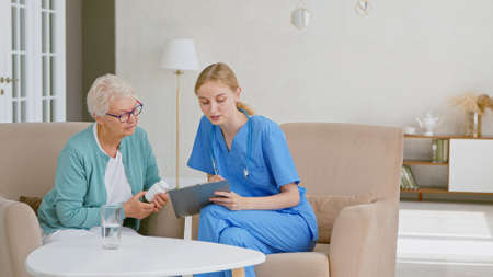 Senior woman holds bottle of pills listening to doctor advice at appointment in light office at modern long term care homeの写真素材