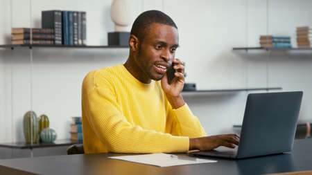 Young man talking on the smartphone while sitting at the desk in home officeの写真素材