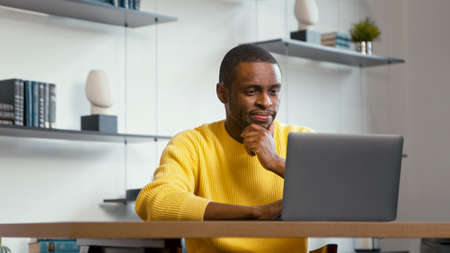 Young man typing on laptop keyboard at the desk at home. Smiling man at workの写真素材